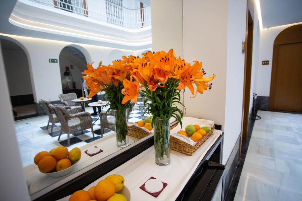 two vases with orange flowers on a table with fruit at Plazuela del Carbón Suites in Cádiz