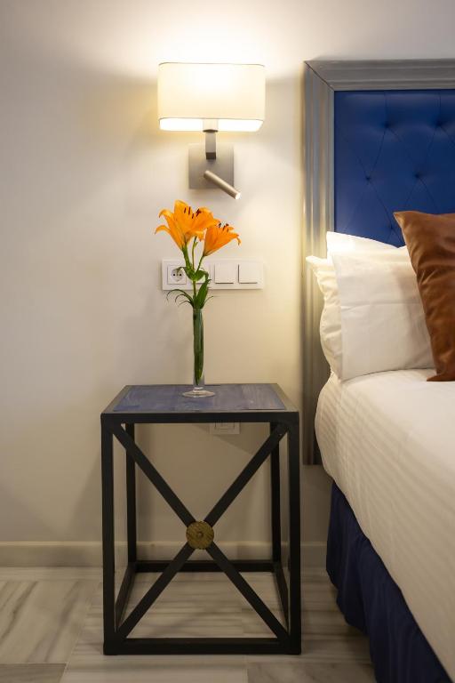 a vase of orange flowers on a table next to a bed at Plazuela del Carbón Suites in Cádiz