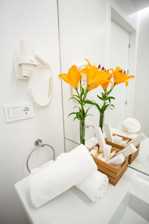 a bathroom sink with a vase of flowers and towels at Plazuela del Carbón Suites in Cádiz