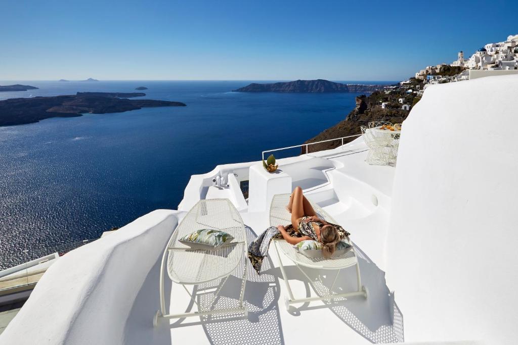 una persona seduta su una sedia su un balcone con vista sull'oceano di Gitsa Cliff Luxury Villa a Imerovigli