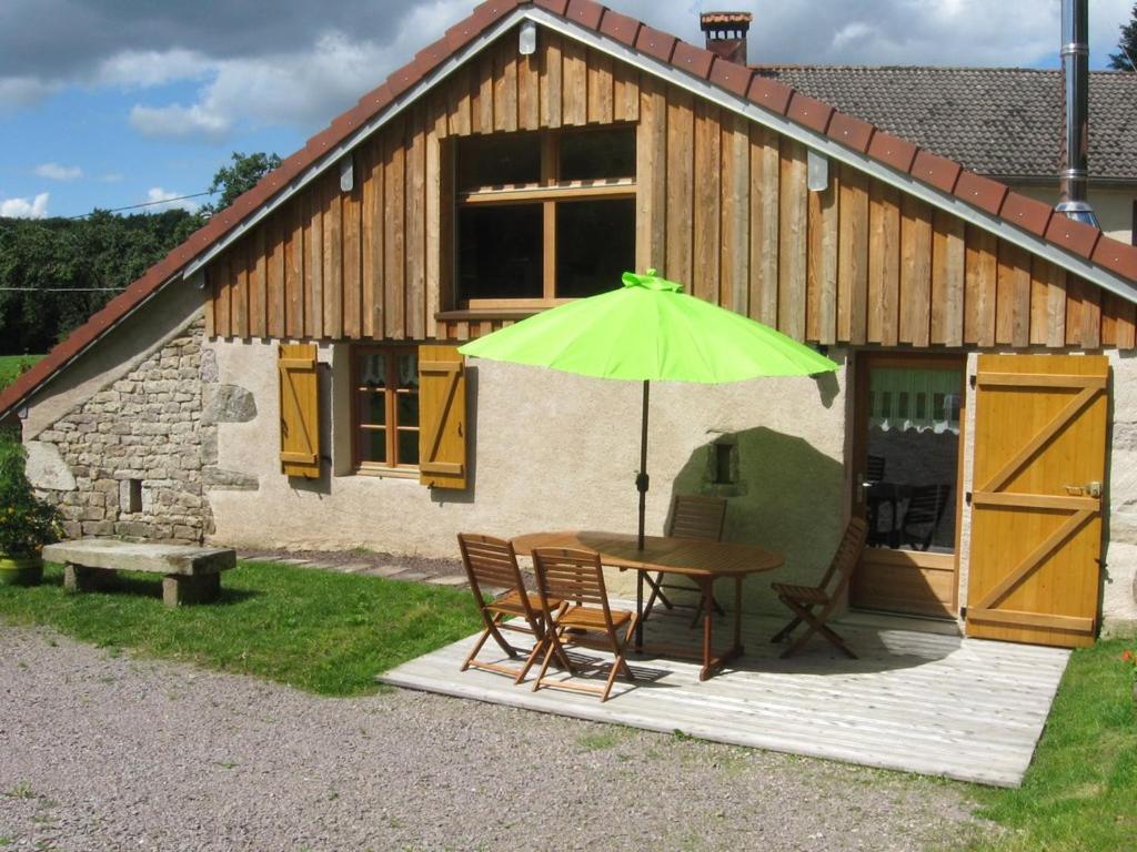 een tafel en stoelen met een groene parasol voor een gebouw bij Gîte des Planches Le Pit in Saint-Bresson