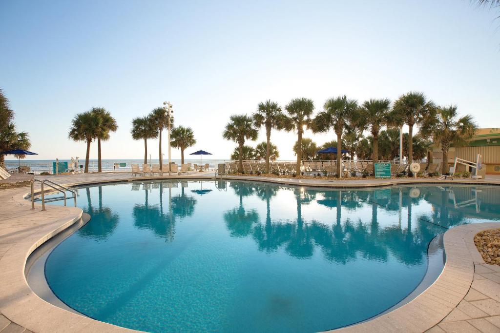 a large swimming pool next to a beach with palm trees at Club Wyndham Ocean Walk in Daytona Beach
