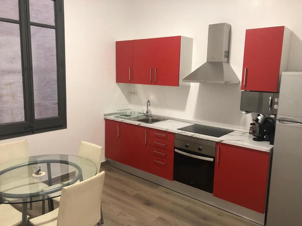 eine Küche mit roten Schränken und einem Glastisch in der Unterkunft Apartament súper centrico, reformado 32 in Tortosa