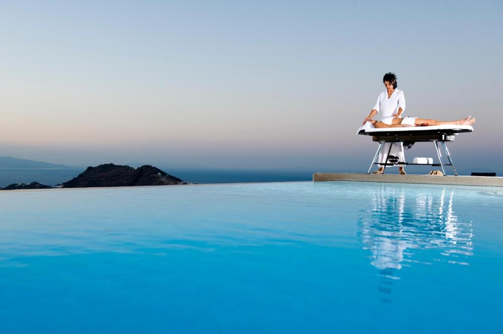 a man sitting at a desk next to a table next to a pool at Avaton Resort And Spa in Imerovigli