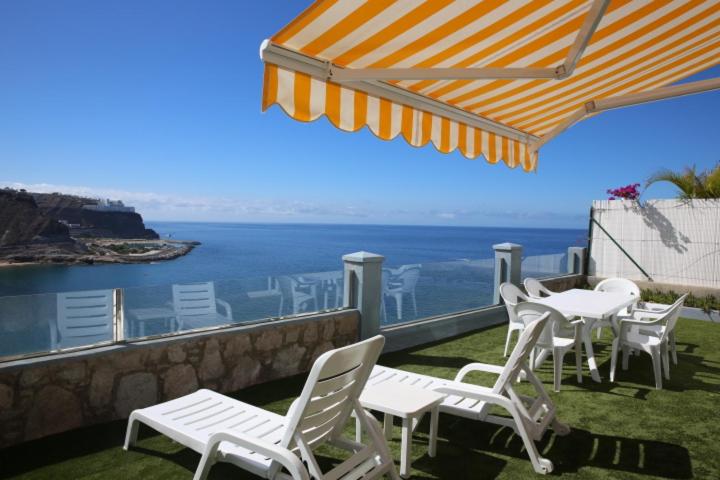 d'une terrasse avec des chaises et des tables blanches et l'océan. dans l'établissement Duplex Playa del Cura beautiful ocean view, à Mogán