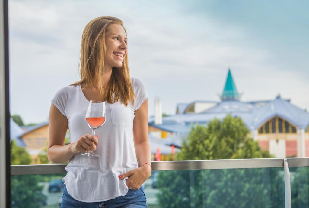 une femme tenant un verre de vin sur un balcon dans l'établissement Berill Suites, à Sárvár