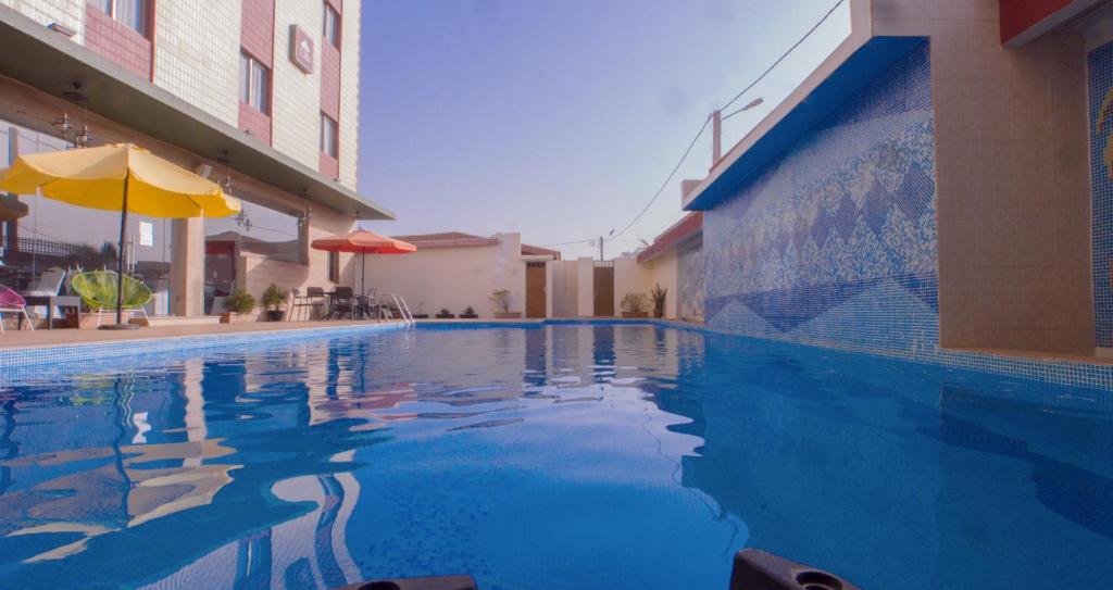 a blue swimming pool with an umbrella next to a building at Hôtel La Rose Blanche Korhogo in Korhogo