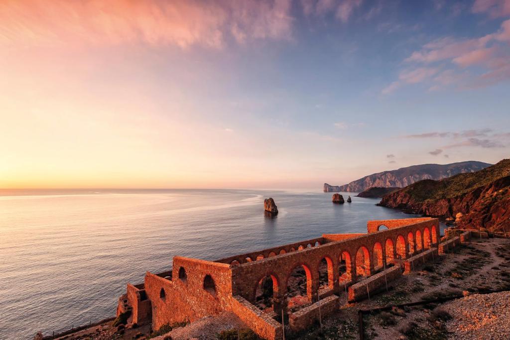 an old stone bridge over the ocean at sunset at Bed and Breakfast Porto Flavia in Iglesias