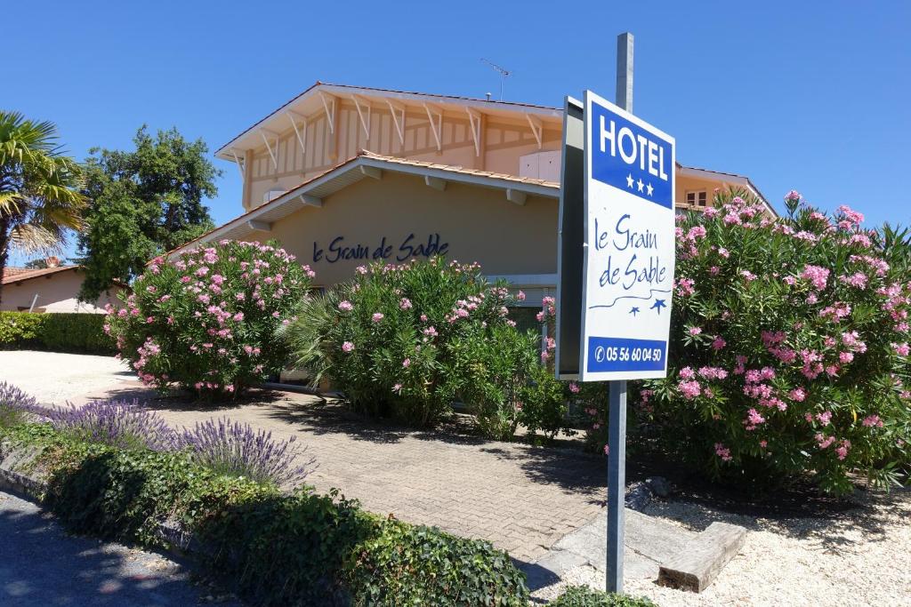 a hotel sign in front of a house with flowers at Hôtel Le Grain de Sable in Arès