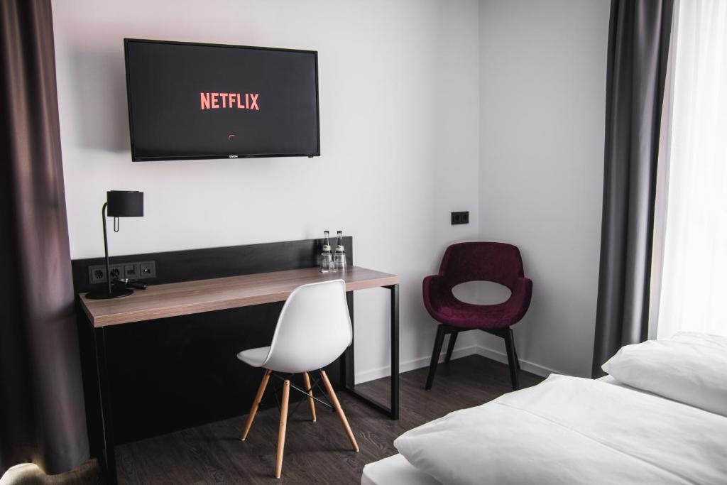 Schlafzimmer mit einem Schreibtisch, einem TV und einem Stuhl in der Unterkunft Hayta Hotel Stuttgart Airport Messe in Filderstadt
