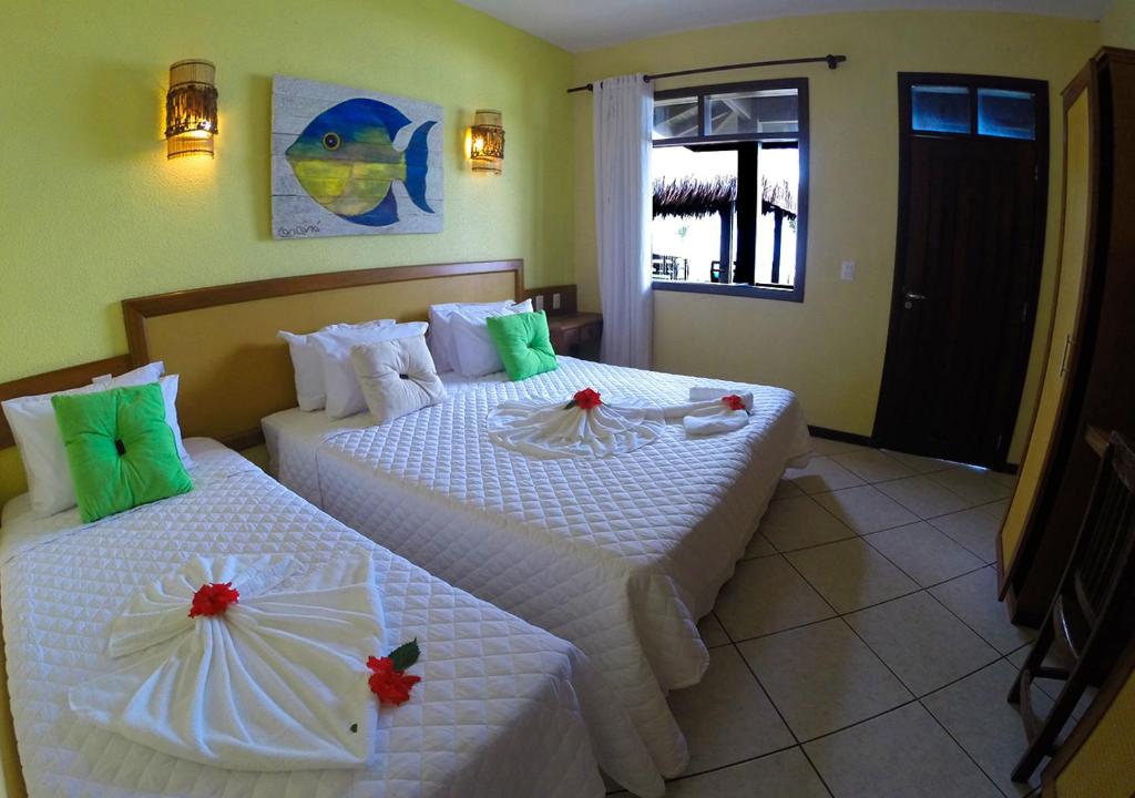two beds in a hotel room with flowers on them at Anauí Pousada in Porto De Galinhas