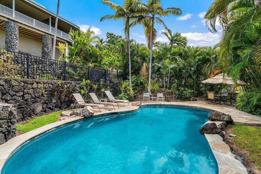 a swimming pool in a yard with chairs and palm trees at Ono Hale in Kailua-Kona