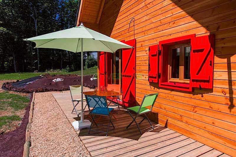 ein Tisch und Stühle mit einem Sonnenschirm auf einem Deck in der Unterkunft Chalet des Noisettes in Murol