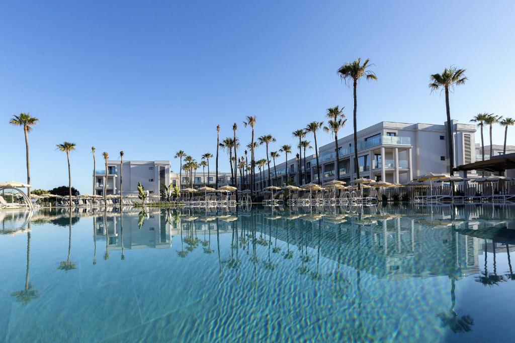 uma grande piscina de água com palmeiras e edifícios em Hipotels Barrosa Park em Chiclana de la Frontera