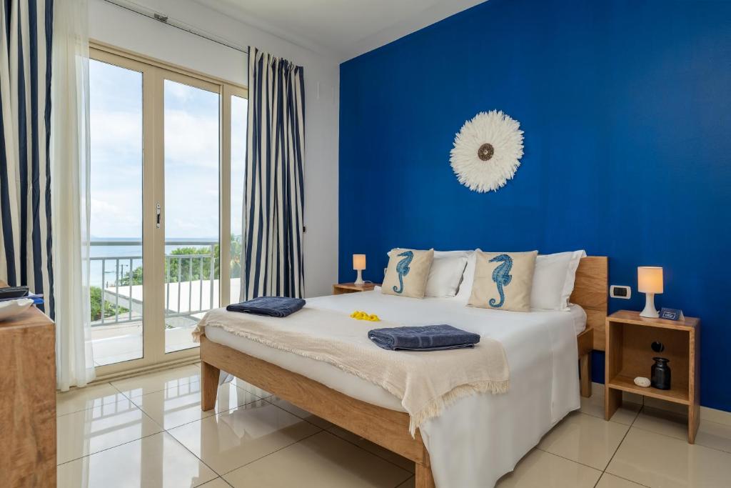 a blue bedroom with a bed and a large window at Villa Roscia in Beau Vallon