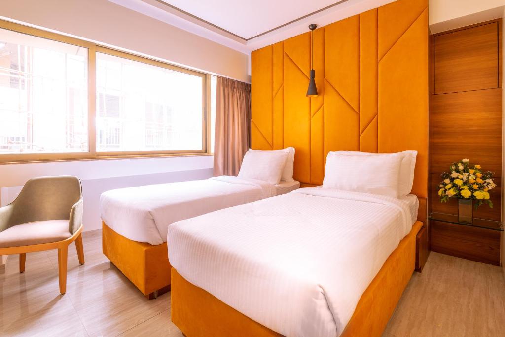 a hotel room with two beds and a chair at Hotel Metropole Inn in Mumbai