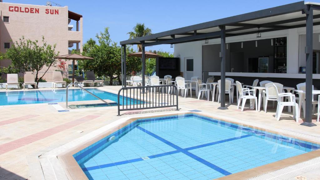 a swimming pool with white chairs and a building at Golden Sun in Tigaki