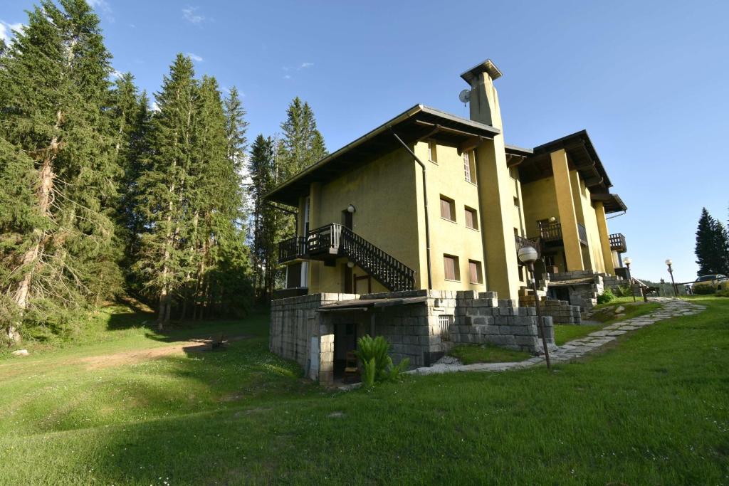 ein großes gelbes Gebäude mit einem Balkon auf einem Grasfeld in der Unterkunft Vagliana appartamento in Madonna di Campiglio