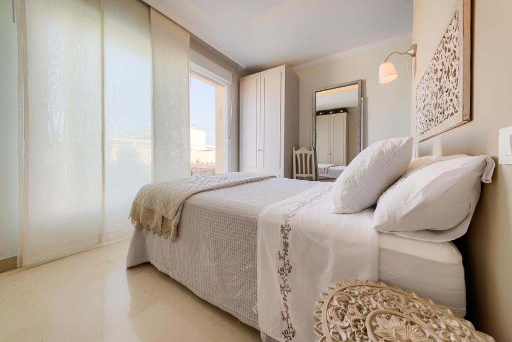 a white bedroom with a large bed and a large window at Ático parque Kotinoussa in Cádiz