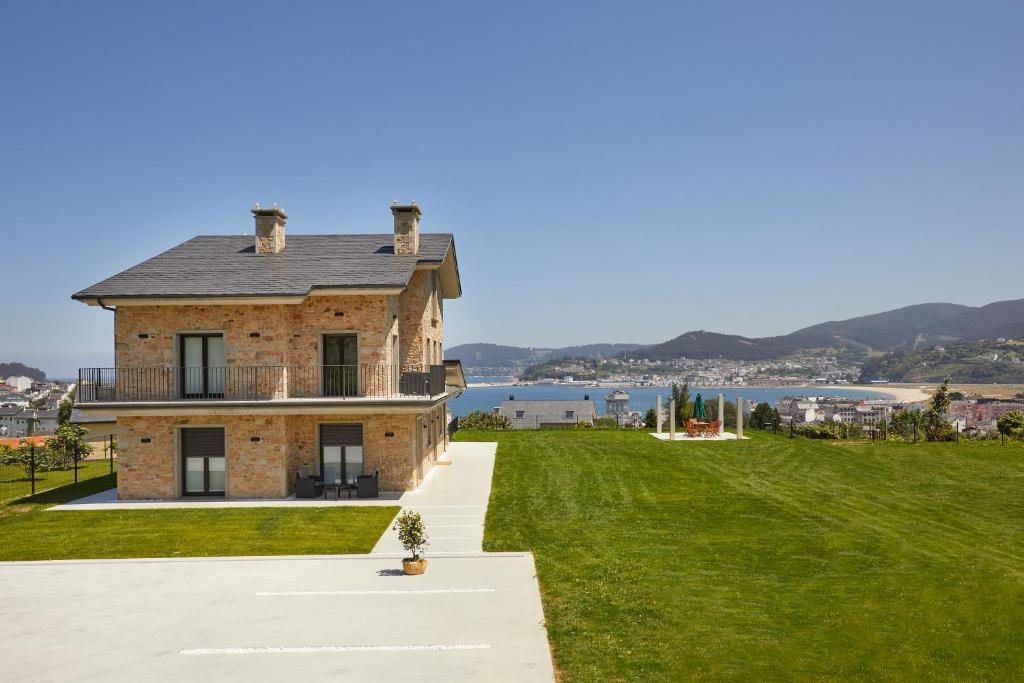 a brick house on a lawn with a view of the water at Apartamentos Arumes do Mar e Montaña - Viveiro in Viveiro