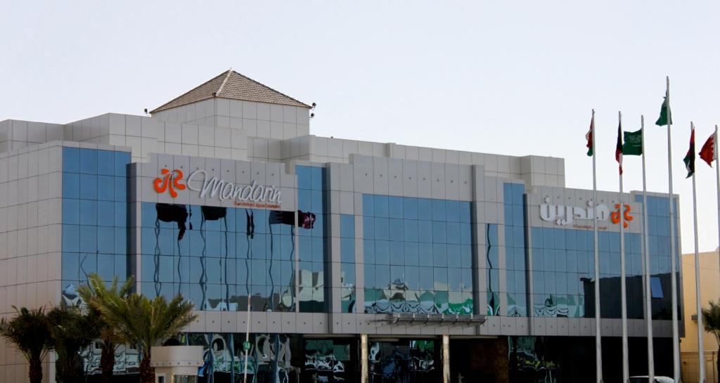 a large glass building with flags in front of it at Mandarin Alshamal Hotel Apartments in Riyadh