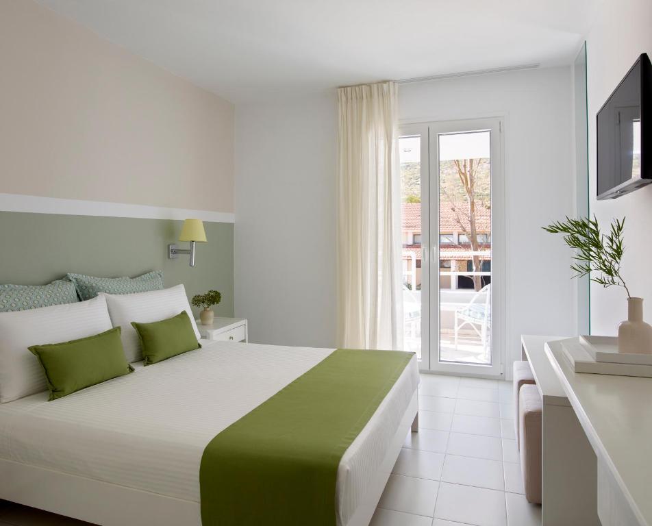 a white bedroom with a large bed and a balcony at Kouros Seasight Hotel in Pythagoreio