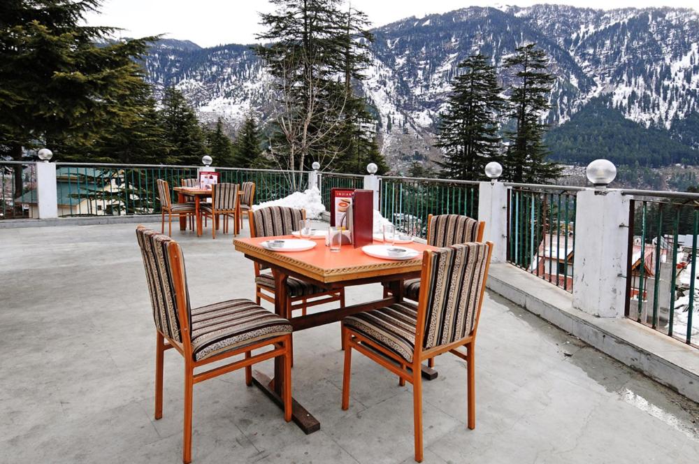 a wooden table and chairs on a patio with mountains at Hotel Greenfields in Manāli