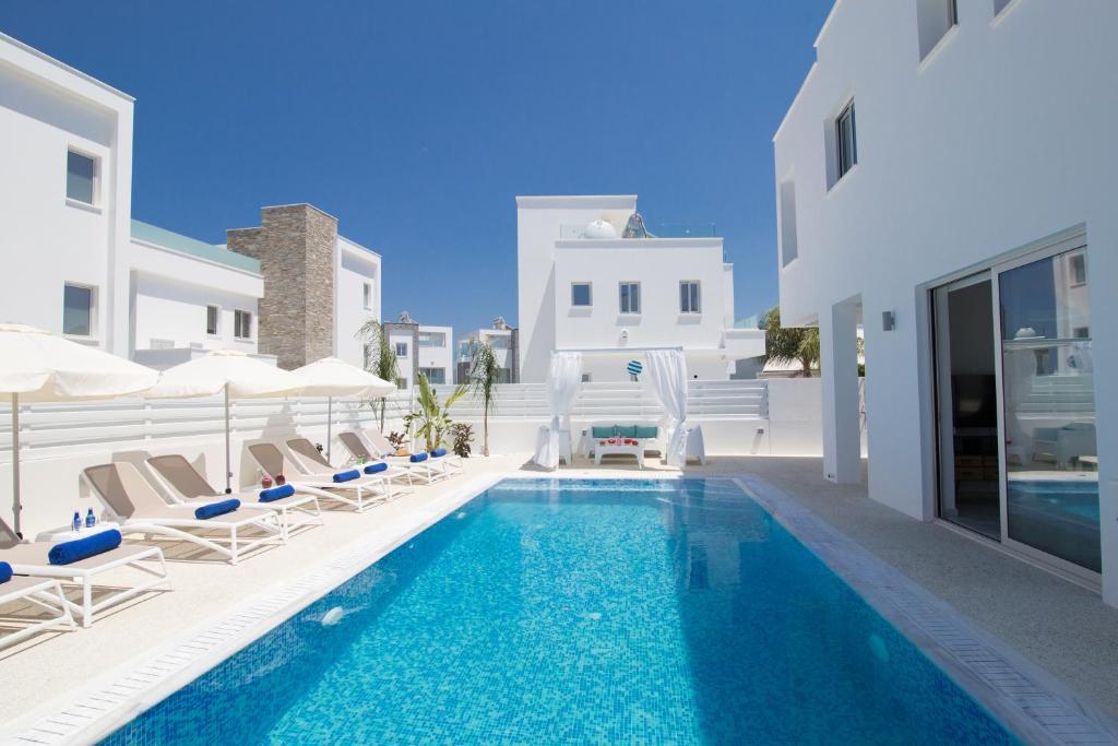 a pool with chairs and umbrellas next to a house at Fig Tree Bay Residences Lantiana Villa 1 in Protaras