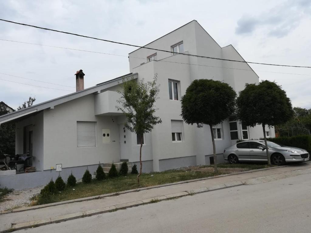 a white house with a car parked in front of it at Apartmani Pause in Niš