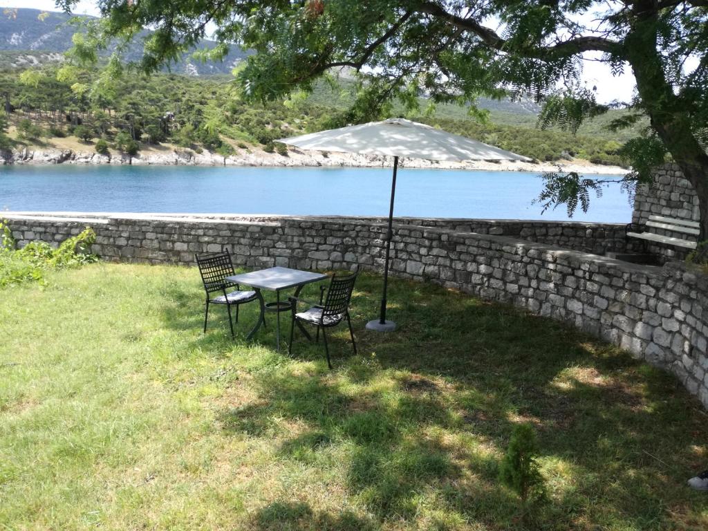 einen Tisch und zwei Stühle im Gras in der Nähe eines Sees in der Unterkunft Apartments Stella Apsyrtides in Osor