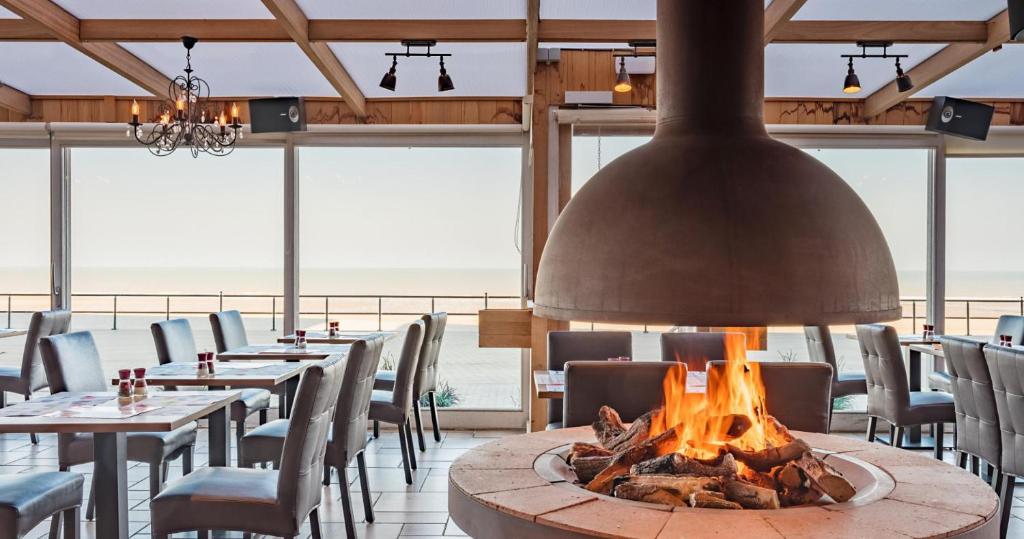 eine Feuerstelle in einem Restaurant mit Tischen und Stühlen in der Unterkunft Hotel De Zeebries in Middelkerke
