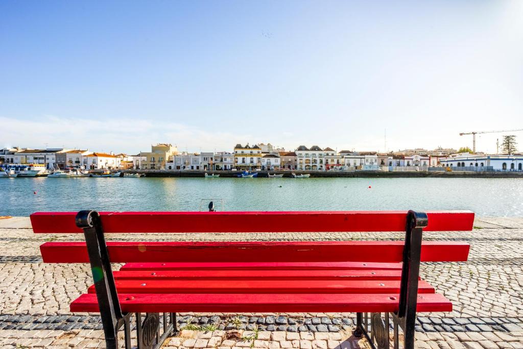 a red bench sitting next to a body of water at Residencial Mares in Tavira