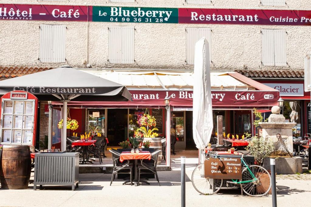 ein Restaurant mit Tischen und Stühlen sowie einem Sonnenschirm und einem Fahrrad in der Unterkunft Hôtel-Restaurant Le Blueberry in Malaucène