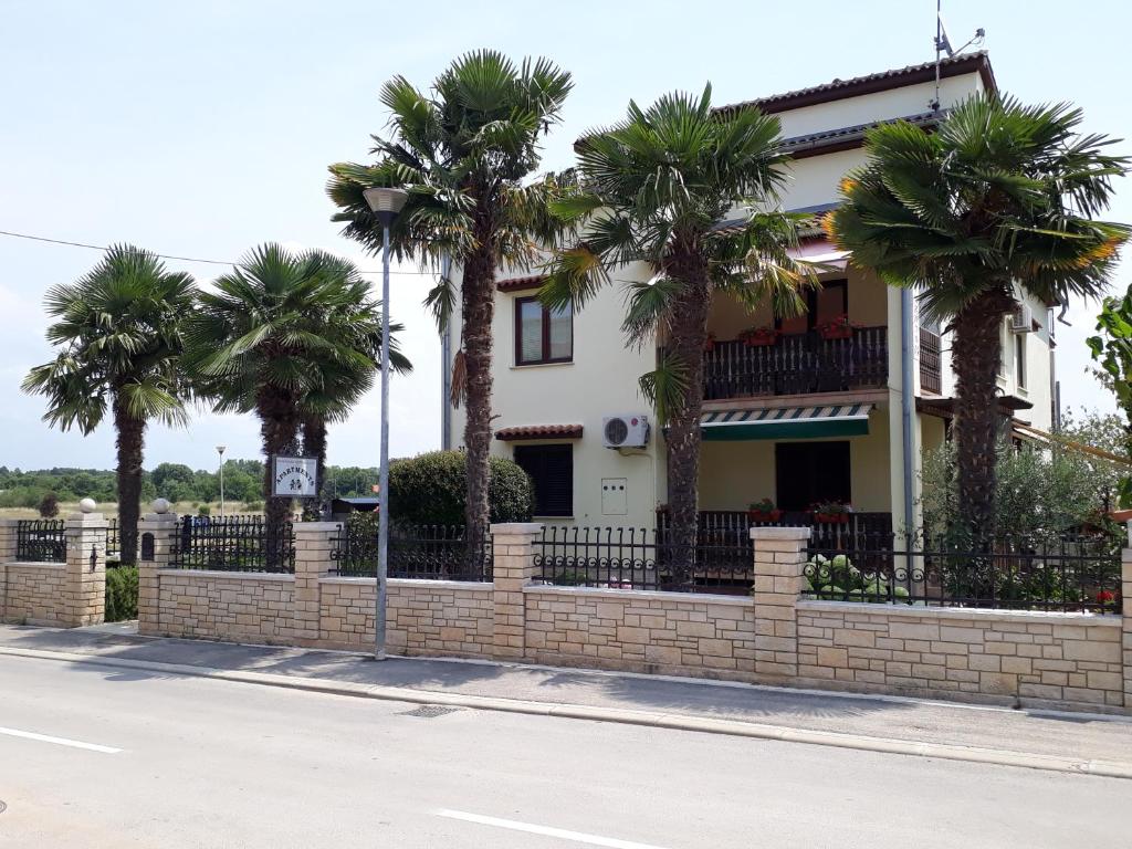 a house with palm trees in front of a brick fence at Funtana Apartments Budinjaš in Funtana