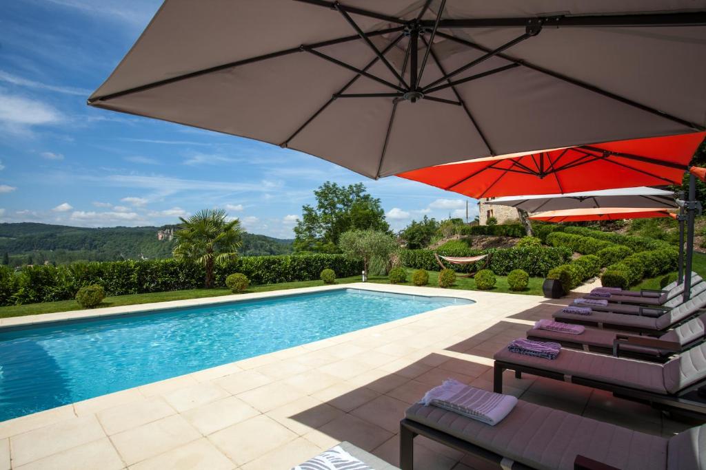 a swimming pool with two umbrellas and chairs next to a pool at Les Hauts de Gageac Maison d'Hôtes de Charme in La Roque-Gageac