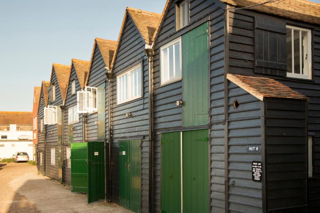 Whitstable Fisherman's Huts في وايتستابل: صف من البيوت الخشبية بأبواب خضراء