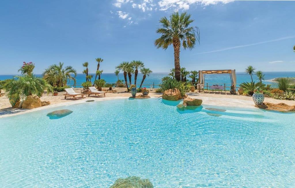 una gran piscina con palmeras y el océano en Casa Vacanze Verdemare con Piscina, en Ribera