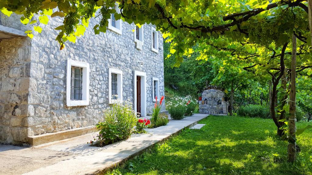 una casa de piedra con un patio verde con un árbol en Guesthouse "Gjin Thana", en Theth