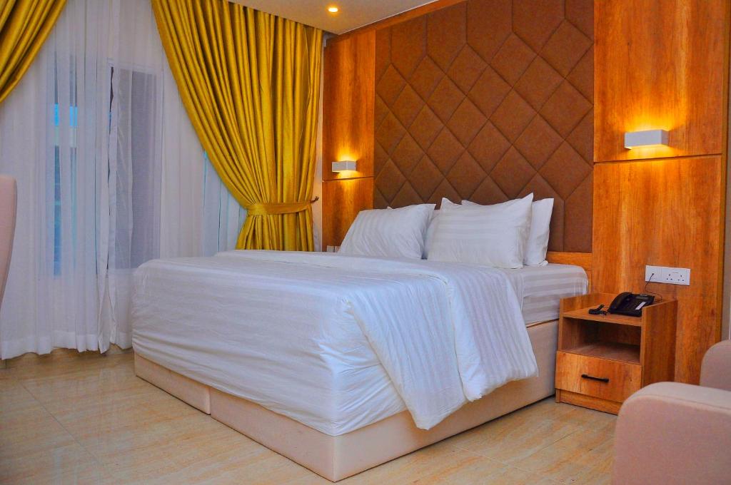 a bedroom with a white bed and a yellow curtain at Lit Suites in Abuja