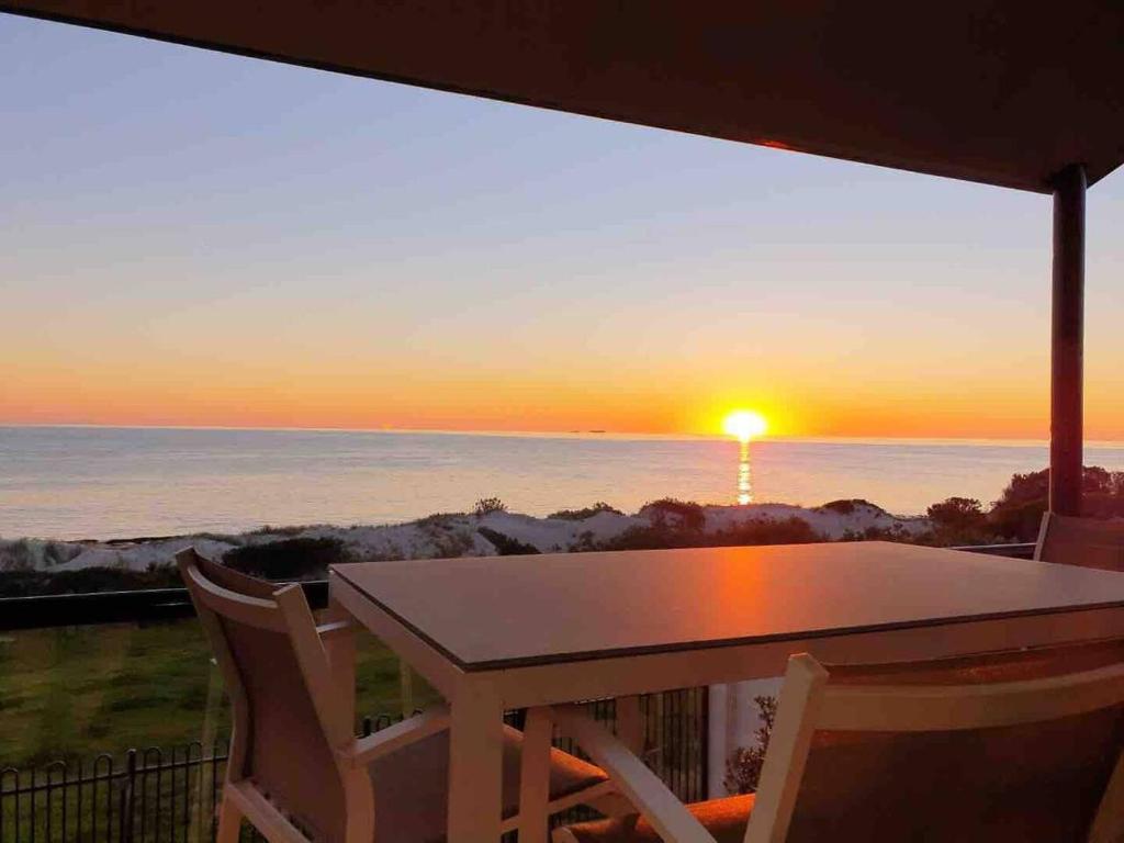a table and chairs on a balcony with a sunset at Luxurious 3 bedroom beachfront - panoramic views in Port Adelaide