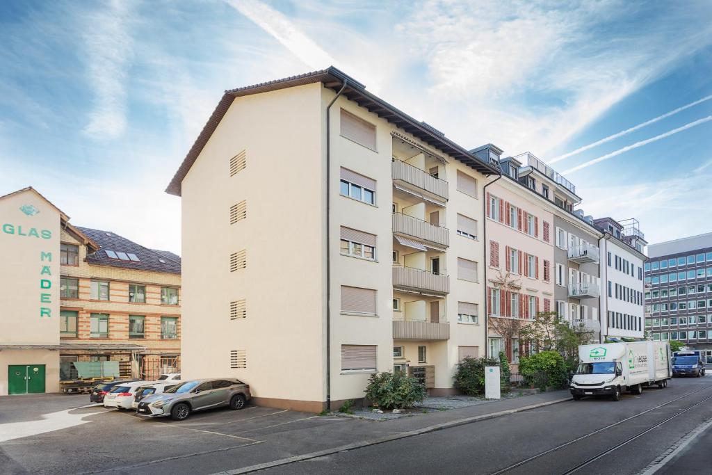 a white building with cars parked in a parking lot at VISIONAPARTMENTS Freyastrasse - contactless check-in in Zürich