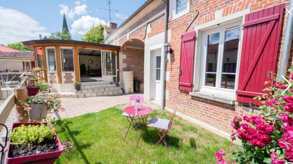 a brick house with red shutters and a table in the yard at Gîte les chèvrefeuilles 3 étoiles in Jonquières