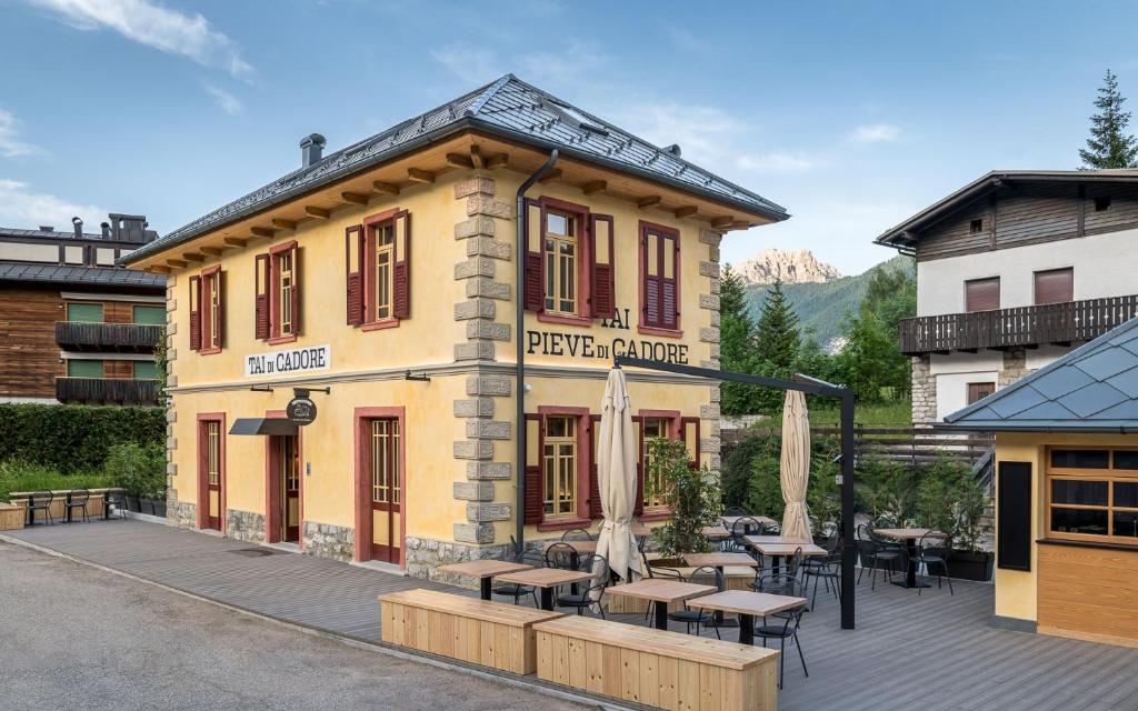 un bâtiment avec des tables et des parasols devant lui dans l'établissement Alla Stazion Locanda nelle Dolomiti, à Pieve di Cadore