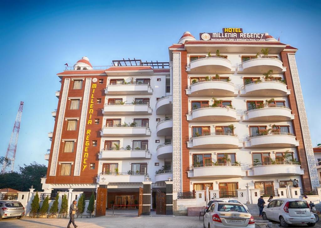 Hotel Millenia Regency Lucknow في لاكناو: مبنى طويل وبه سيارات متوقفة أمامه
