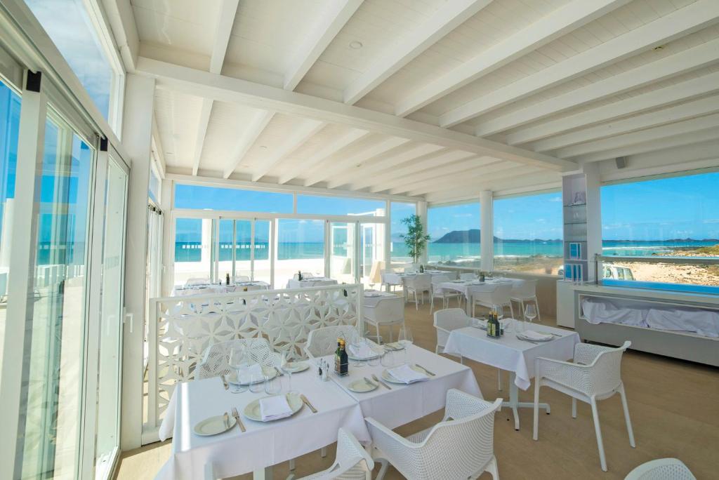 a dining room with white tables and chairs and windows at Hotel Boutique TAO Caleta Mar in Corralejo