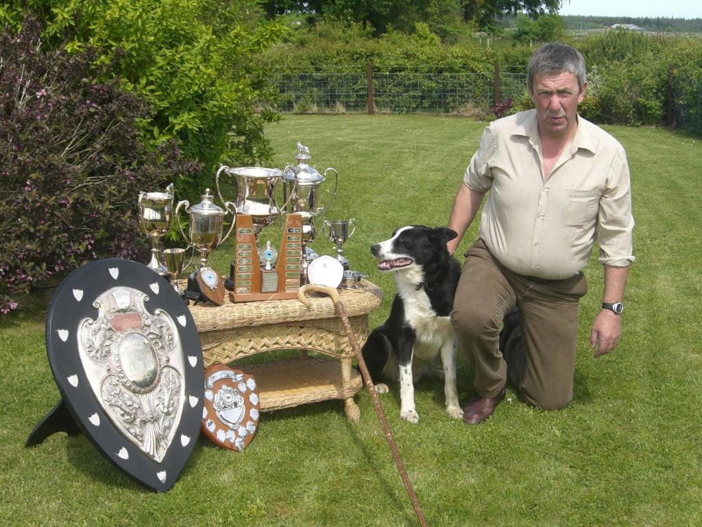 um homem ajoelhado ao lado de um cão ao lado de uma mesa em Leanach Farm em Inverness