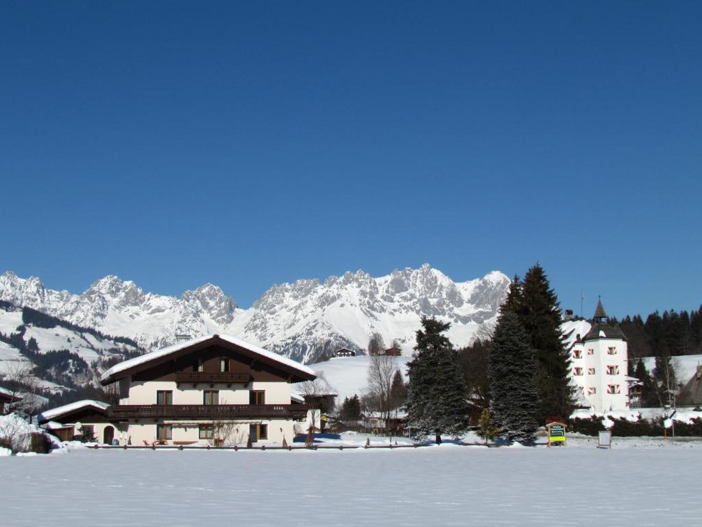 un edificio en la nieve con montañas en el fondo en Ferienwohnungen - Haus Zierl, en Reith bei Kitzbühel