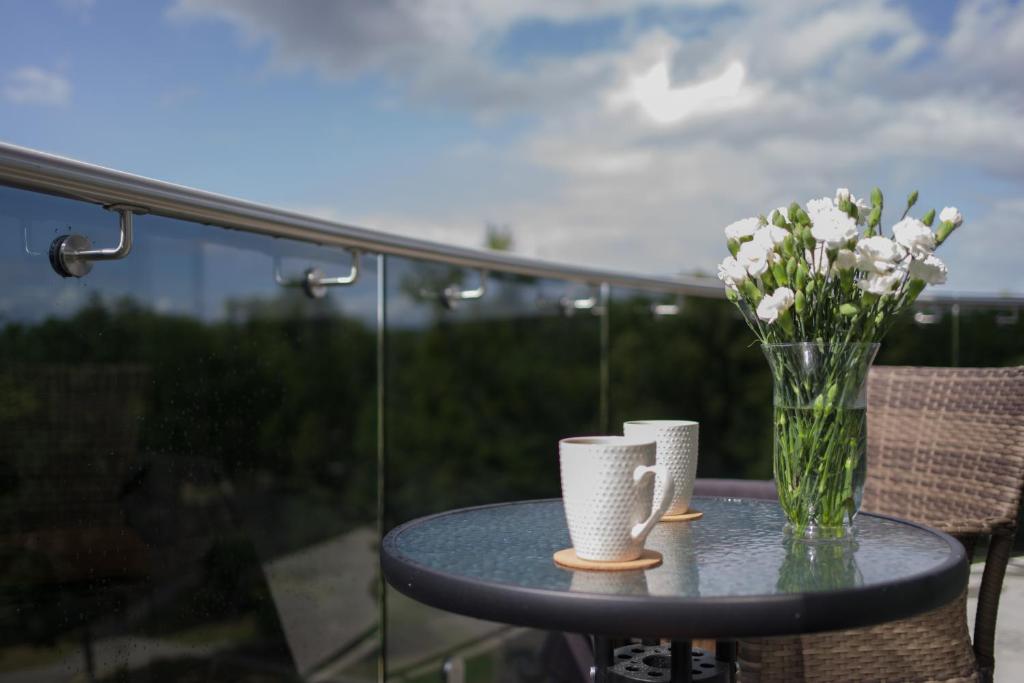 a table with a vase of flowers and two cups at Luxury Apartments in Druskininkai