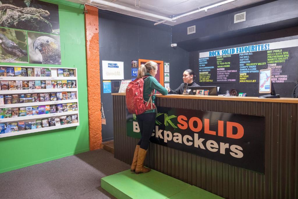 une femme inscrite à un registre de caisse dans un magasin dans l'établissement Rock Solid Backpackers Rotorua, à Rotorua
