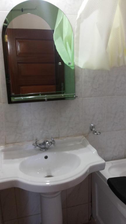 a bathroom with a sink and a mirror and a tub at Hotel Dot Com Entebbe in Entebbe